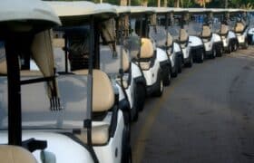 Row of white golf carts awaiting customization at Flamingo Custom Carts